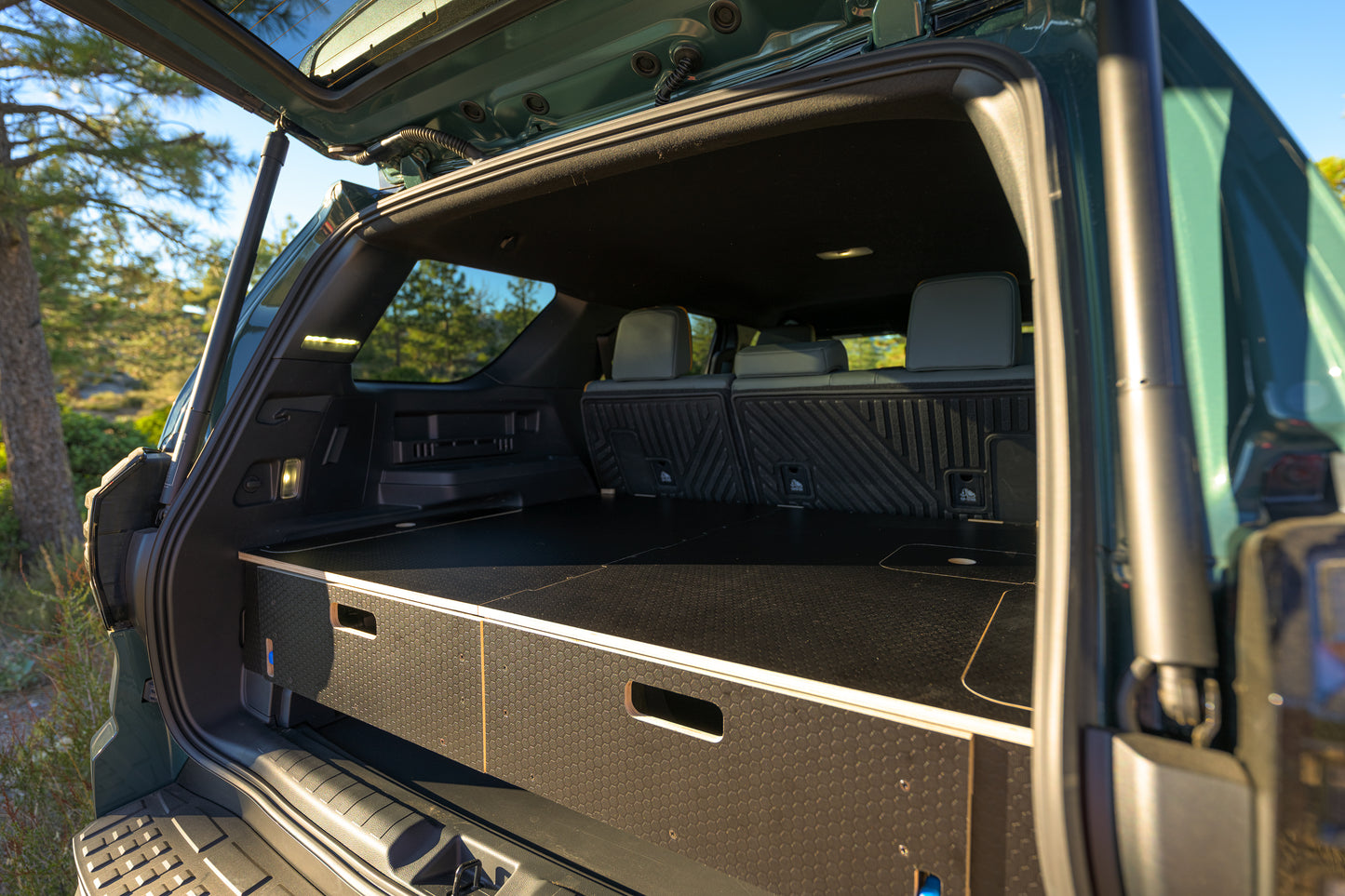 SUV rear cargo area with custom wood storage drawers and seats folded down.