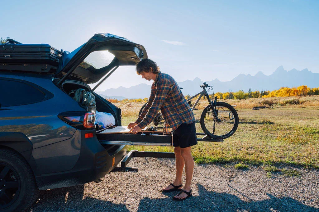 Man using vehicle pull-out drawer storage system outdoors with bike rack and mountain view