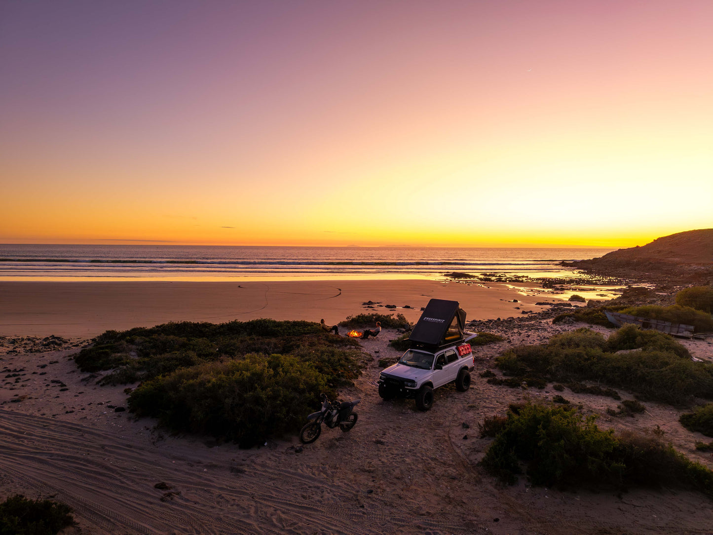 Off-road vehicle with rooftop tent on sandy beach at sunset, coastal camping scene
