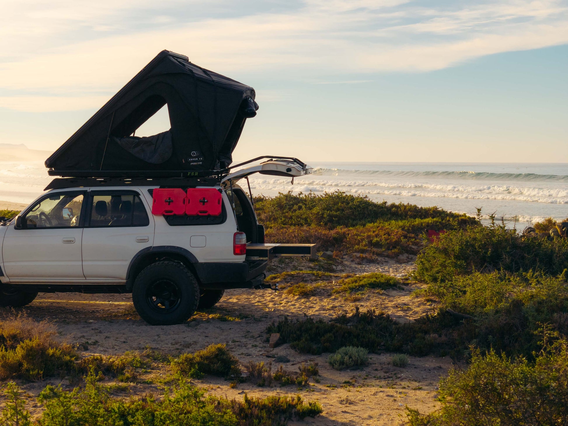 SUV with rooftop tent and vehicle storage drawers parked at coastal campsite