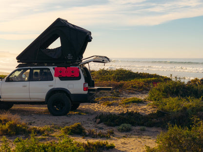 SUV with rooftop tent and vehicle storage drawers parked at coastal campsite