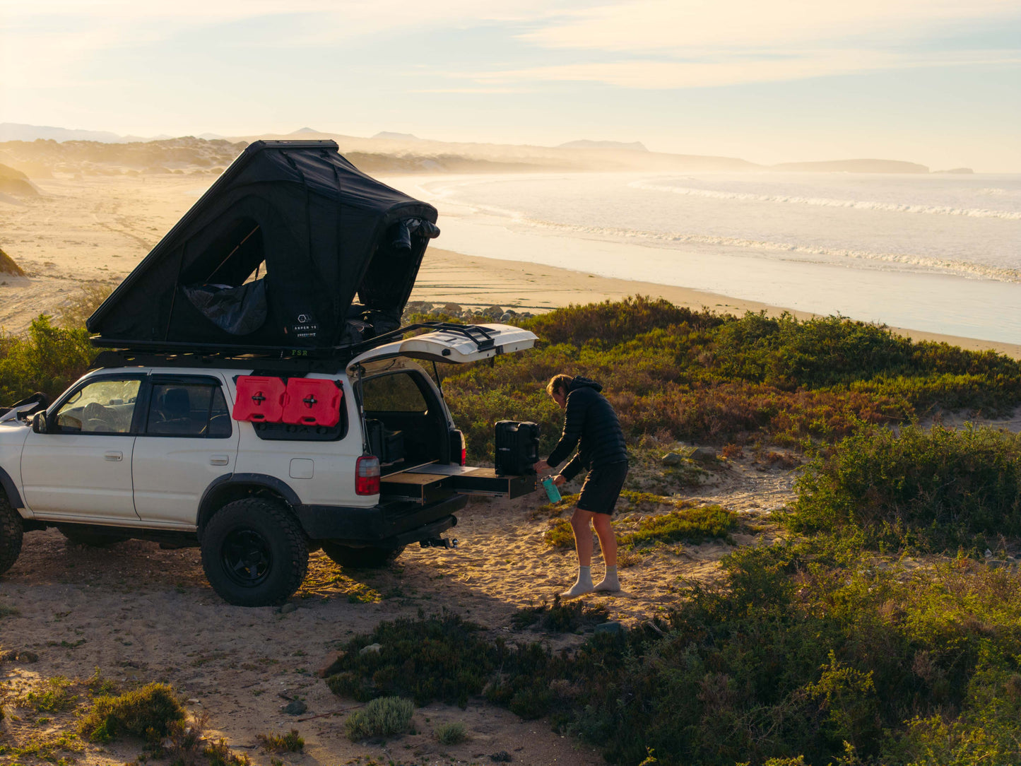 SUV with rooftop tent and rear drawer storage system parked on a beach at sunset