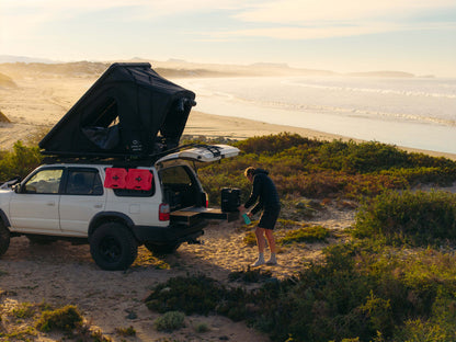 SUV with rooftop tent and rear drawer storage system parked on a beach at sunset