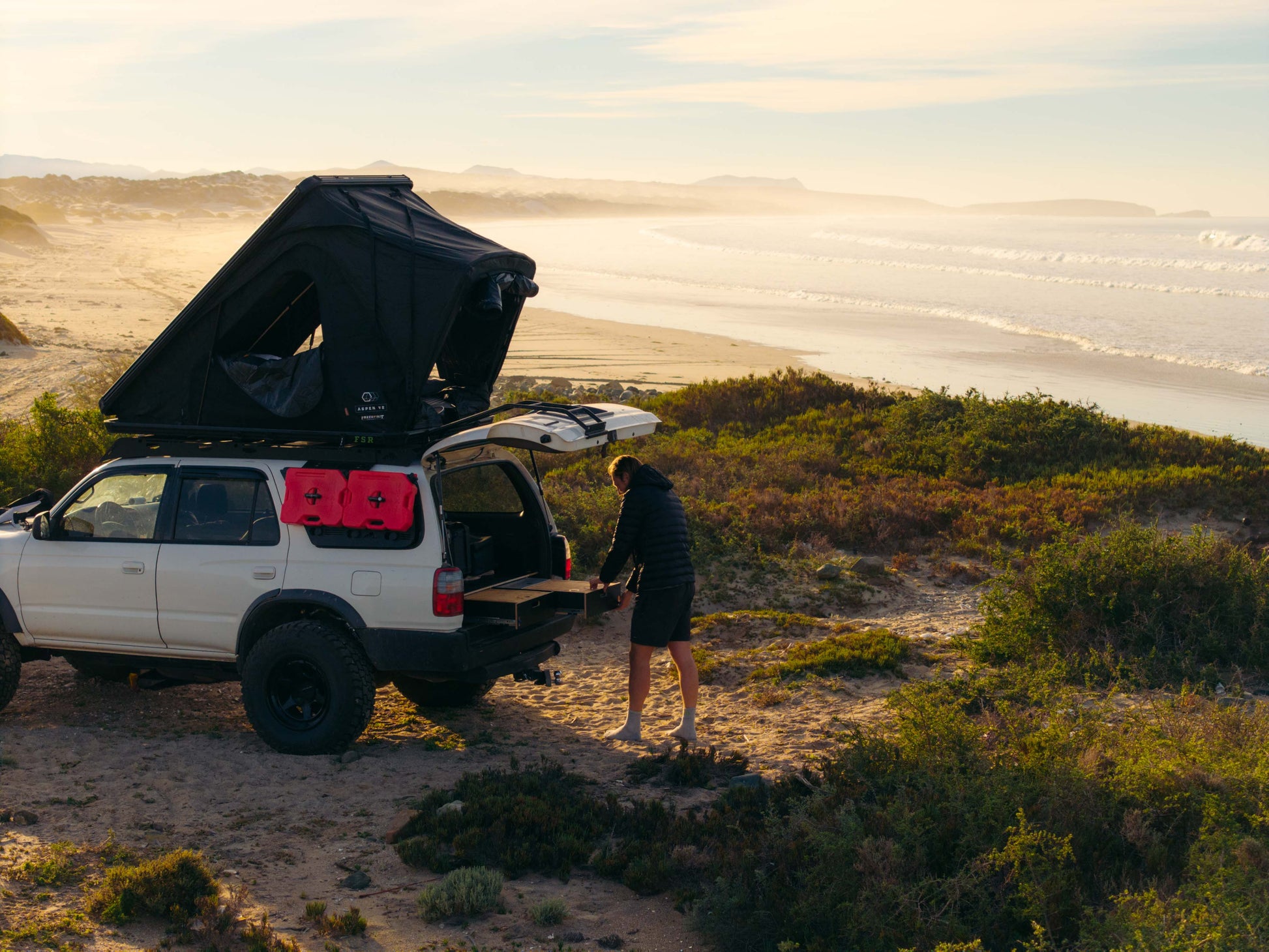 SUV with rooftop tent and vehicle drawer storage system on a beach at sunset