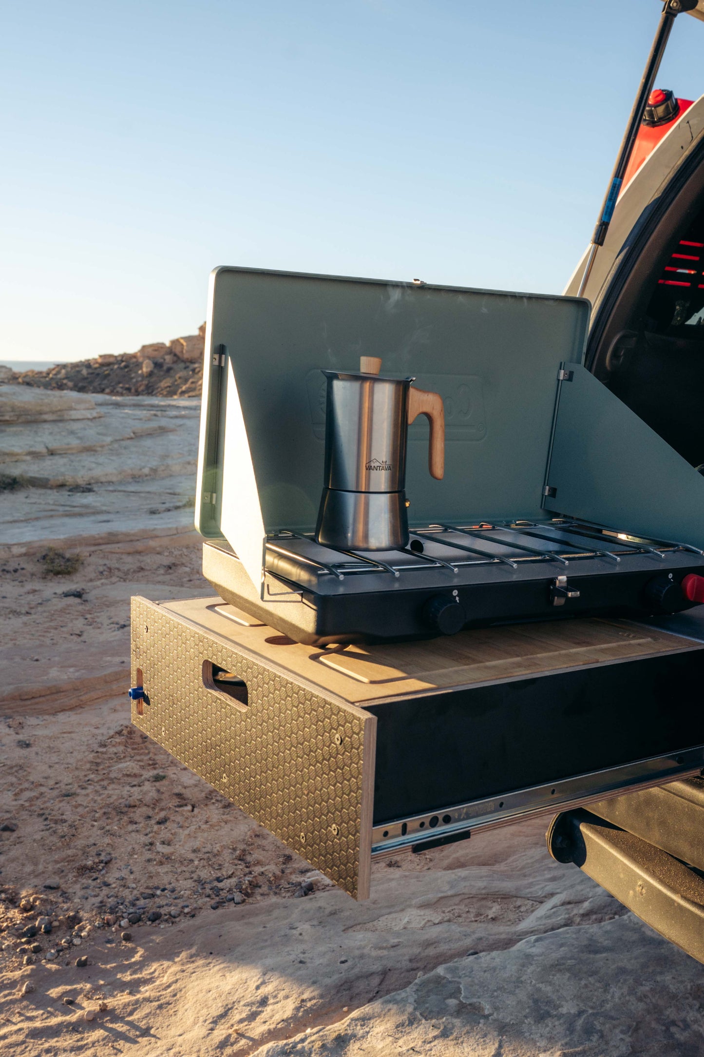 Vehicle drawer system with pull-out kitchen and camp stove in a rocky outdoor setting