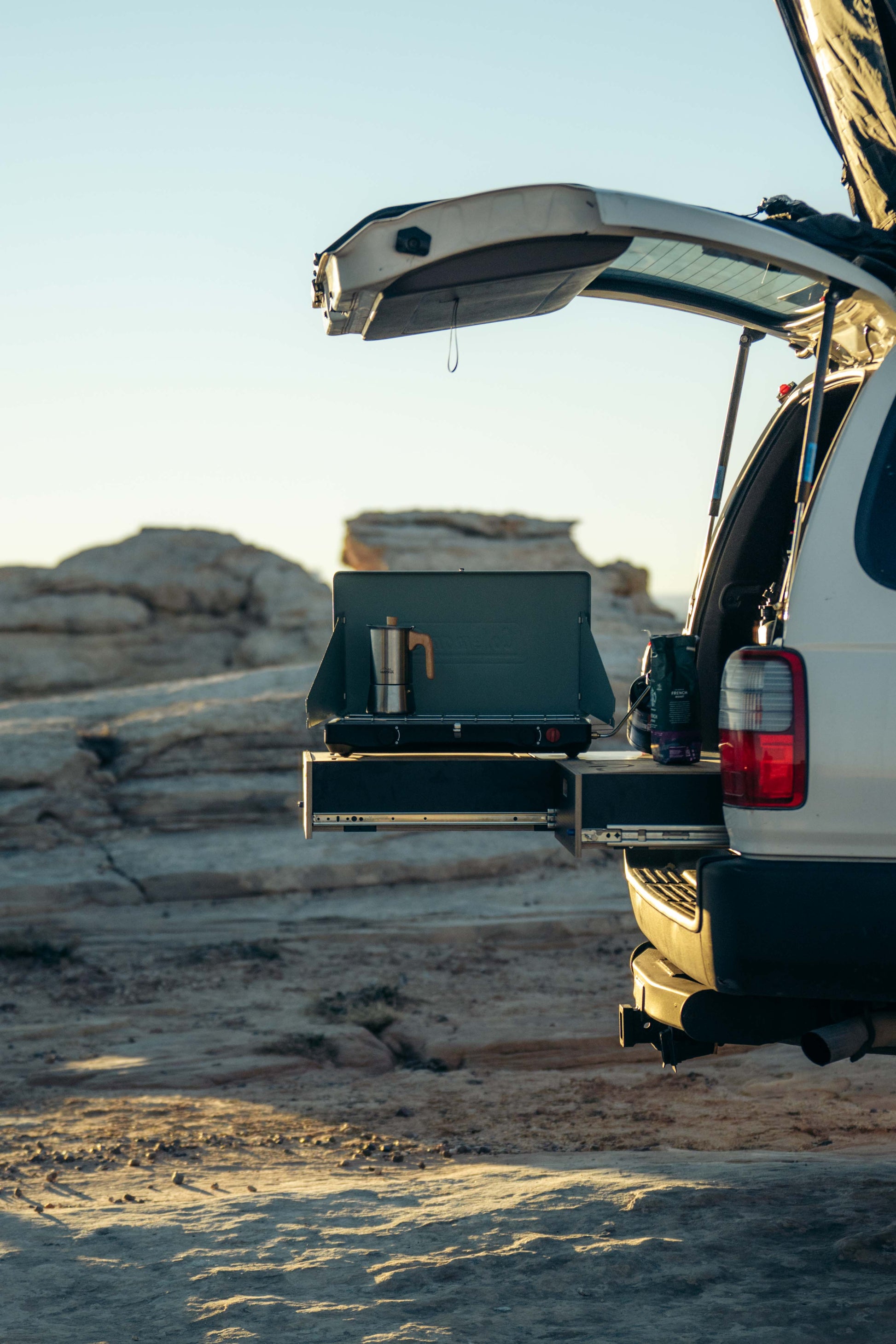 SUV with rear drawer system open, camping stove setup, rocky outdoor setting