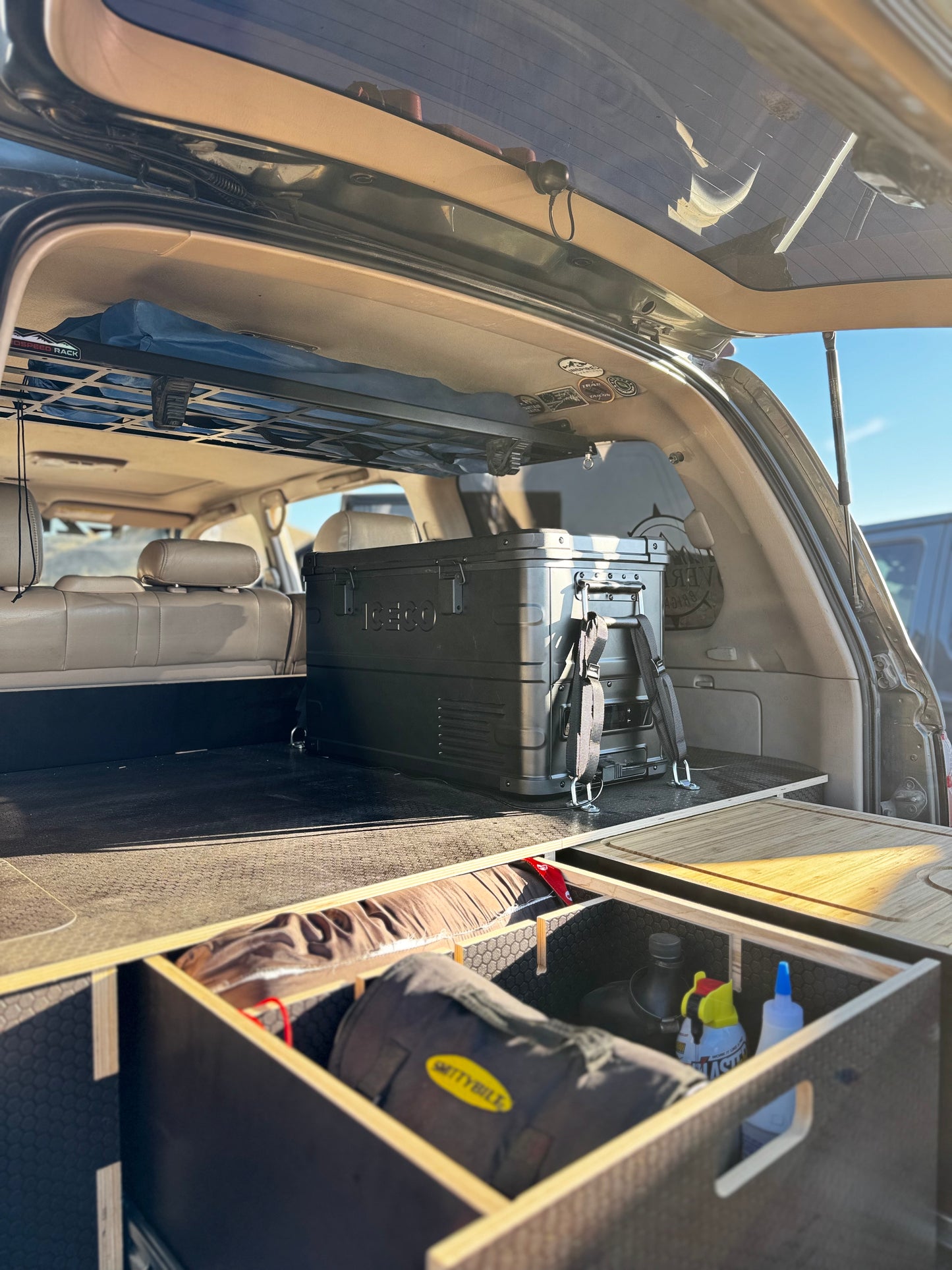 Vehicle cargo area with custom wooden drawer system and storage boxes inside trunk.
