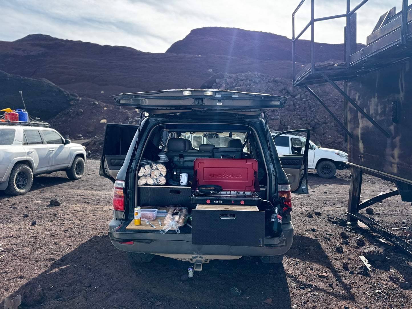 SUV rear open displaying outdoor vehicle drawer storage system with camping gear in rocky landscape