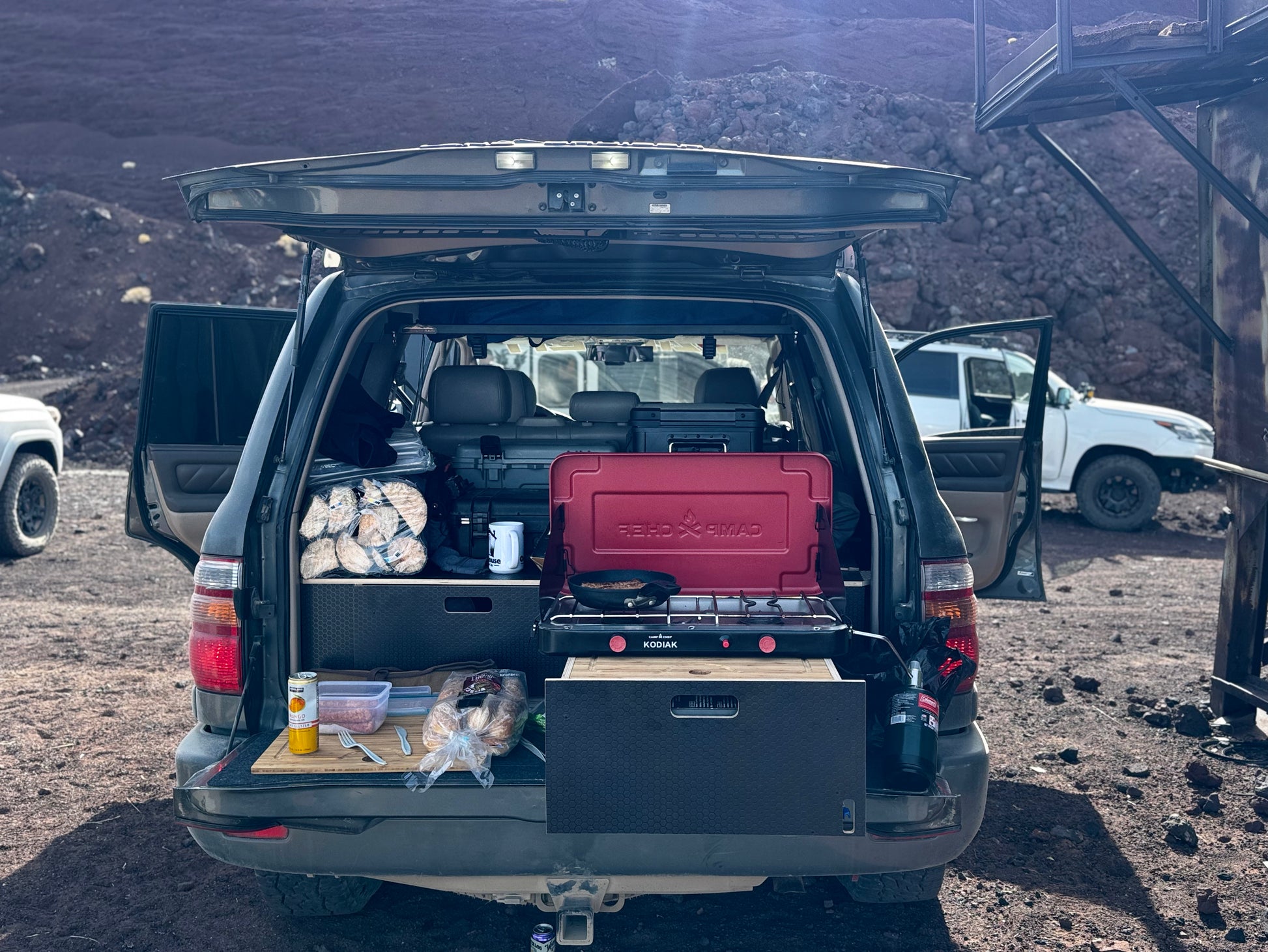 SUV trunk open with custom drawer system, camping stove, and outdoor storage setup