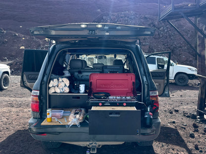 SUV trunk open with custom drawer system, camping stove, and outdoor storage setup