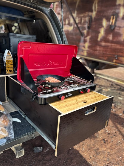 Vehicle storage drawer system with pull-out camp kitchen and portable stove in use outdoors
