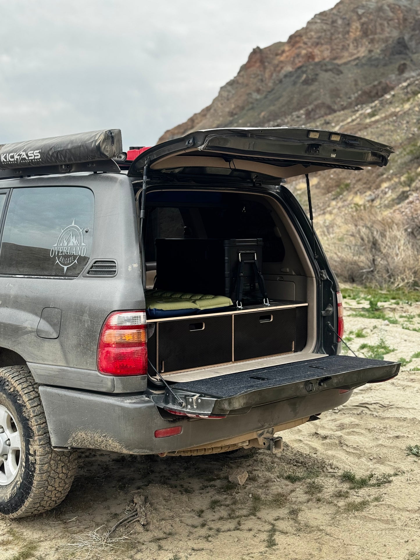 SUV with custom wood drawer storage system for camping, parked outdoors on dirt terrain