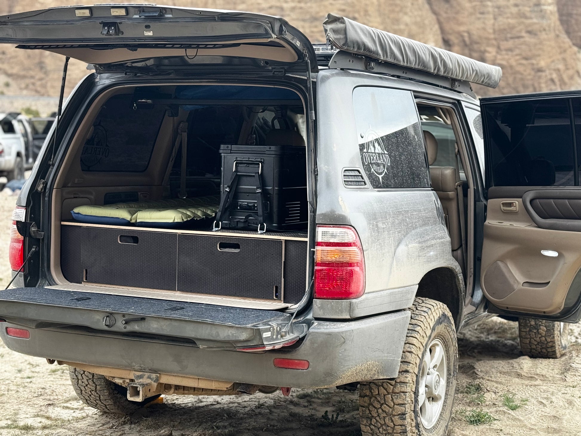 SUV with rear drawer storage system, camping gear, and awning in an outdoor setting