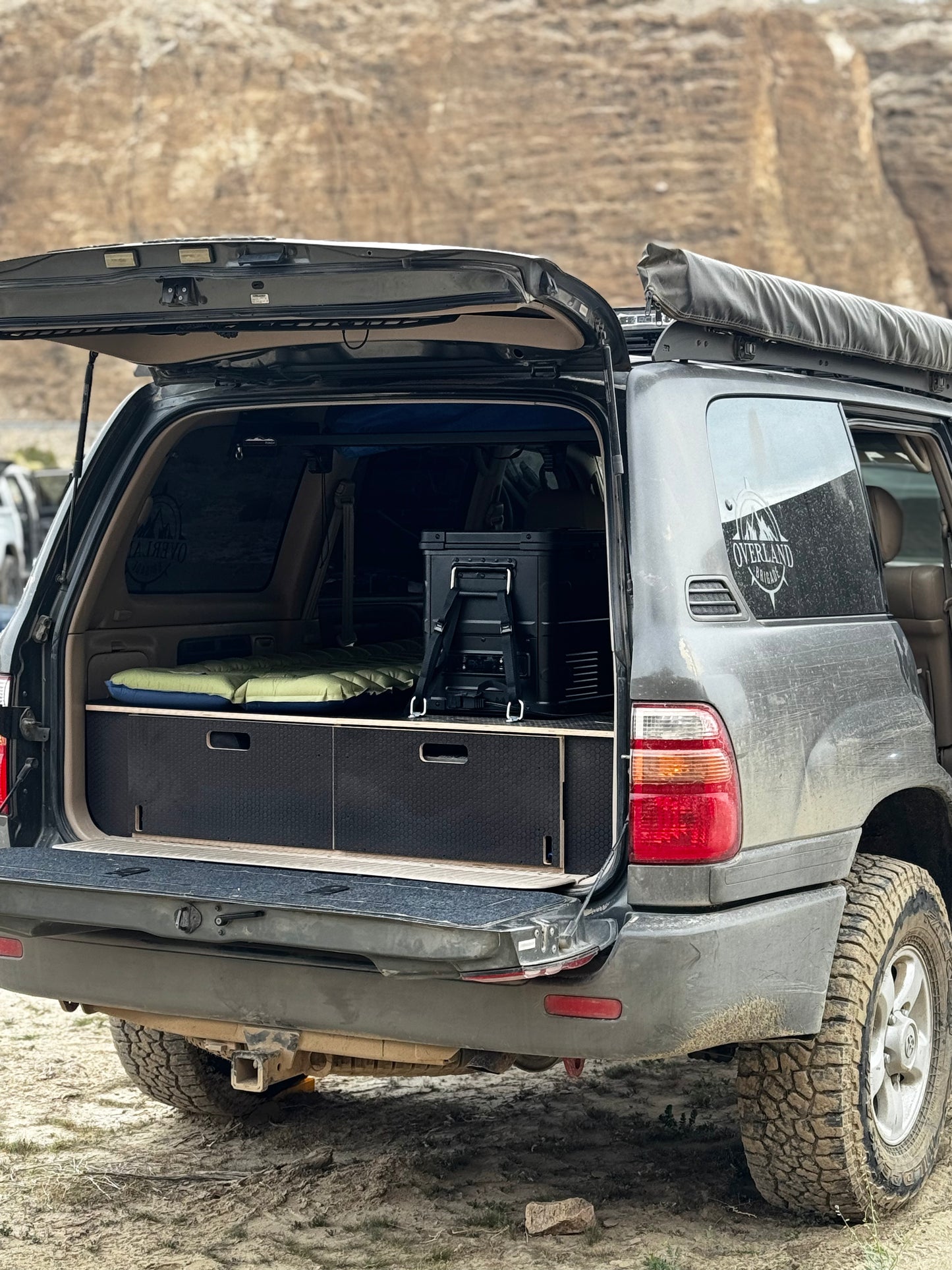 SUV with rear hatch open, showing built-in vehicle drawer storage system and camping gear