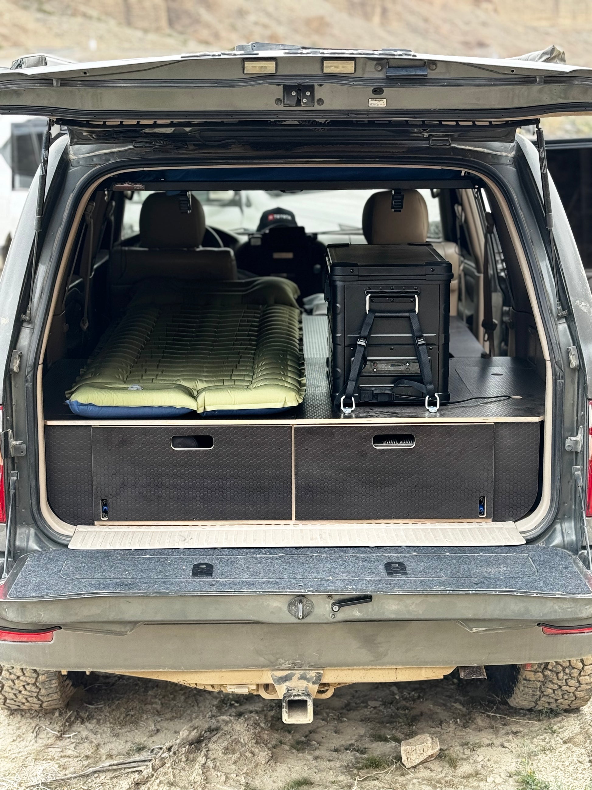 SUV rear cargo area with custom drawer system, storage boxes, and camping bed setup