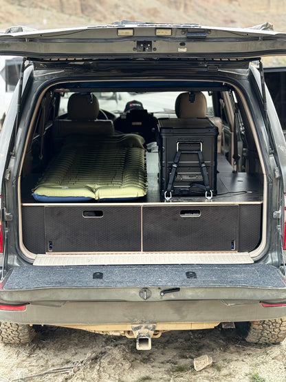 SUV rear cargo area with custom drawer system, storage boxes, and camping bed setup