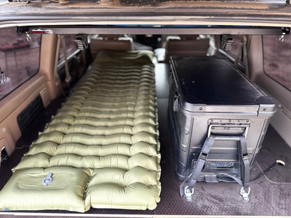SUV trunk with inflatable camping mattress and black storage box for vehicle organization.