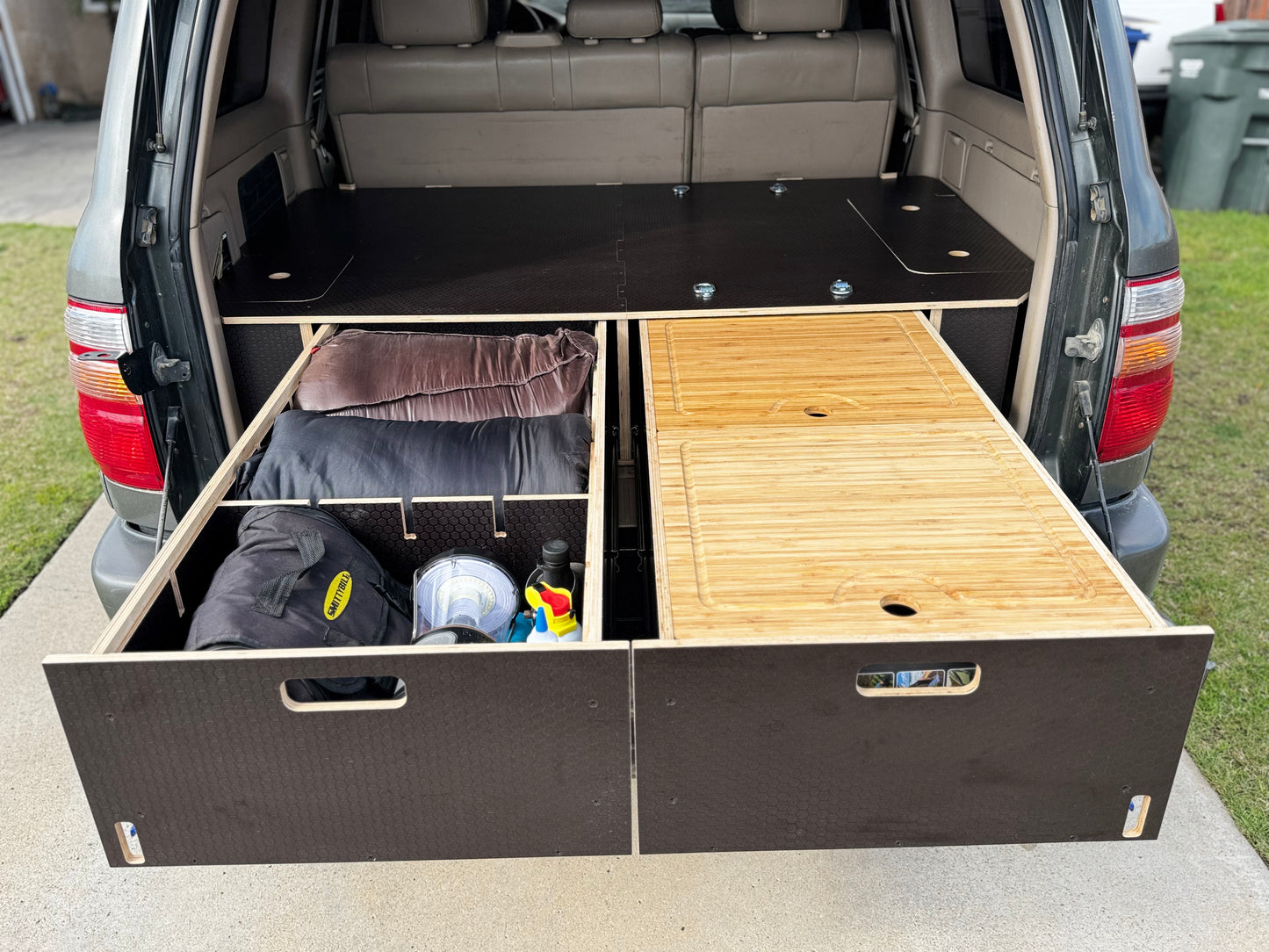 SUV trunk with custom wood drawer storage system, organized with camping gear and supplies.