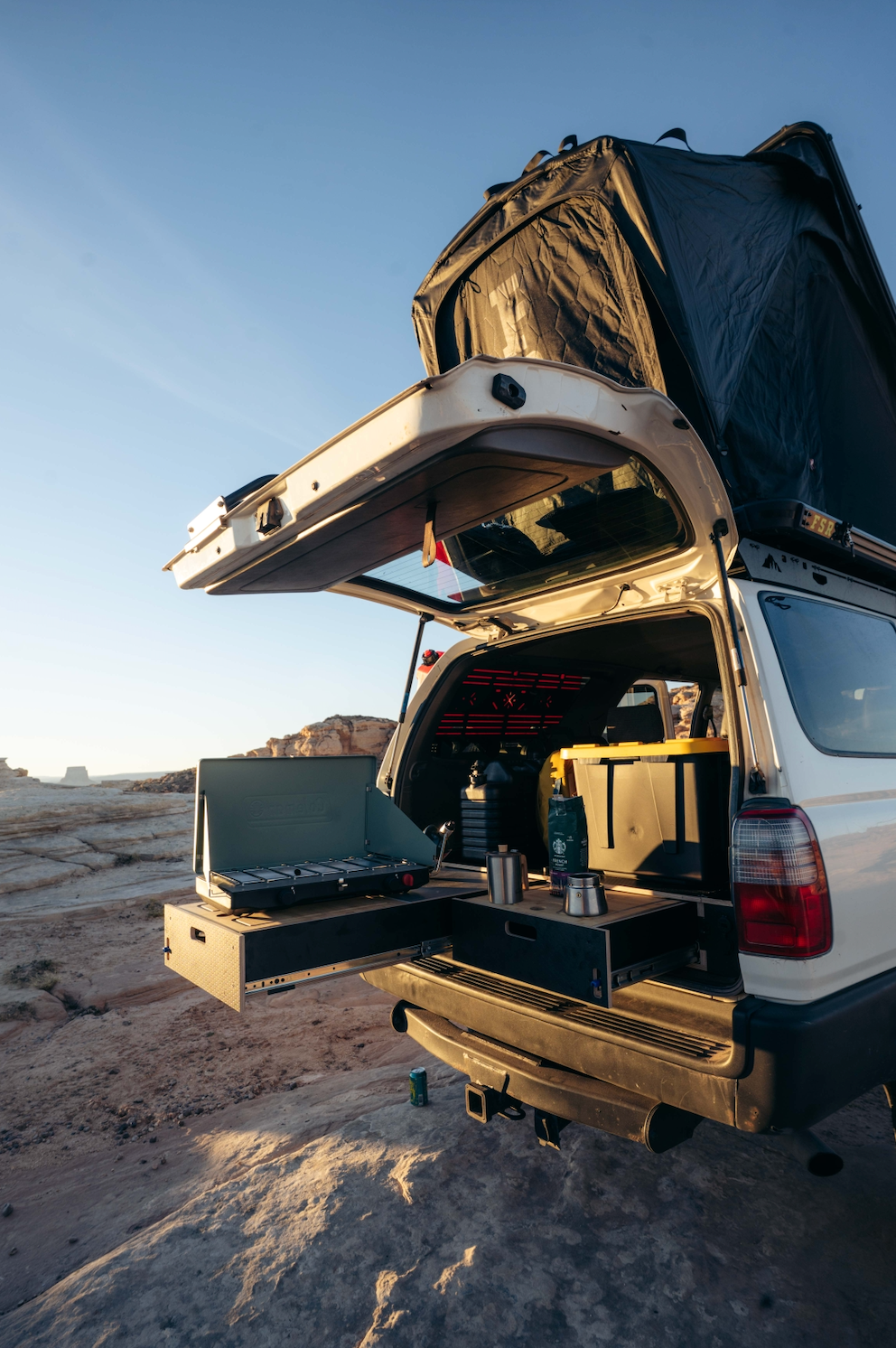 Vehicle with rear storage drawer system, camping kitchen setup, and rooftop tent outdoors