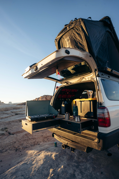 Vehicle with rear storage drawer system, camping kitchen setup, and rooftop tent outdoors