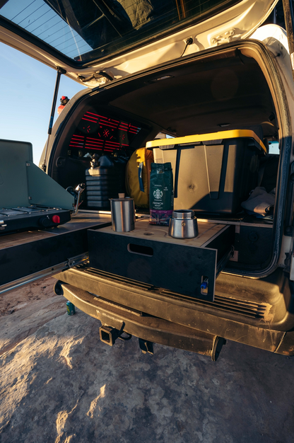 SUV with open trunk showing vehicle storage drawer system, camping stove, and gear organizer.