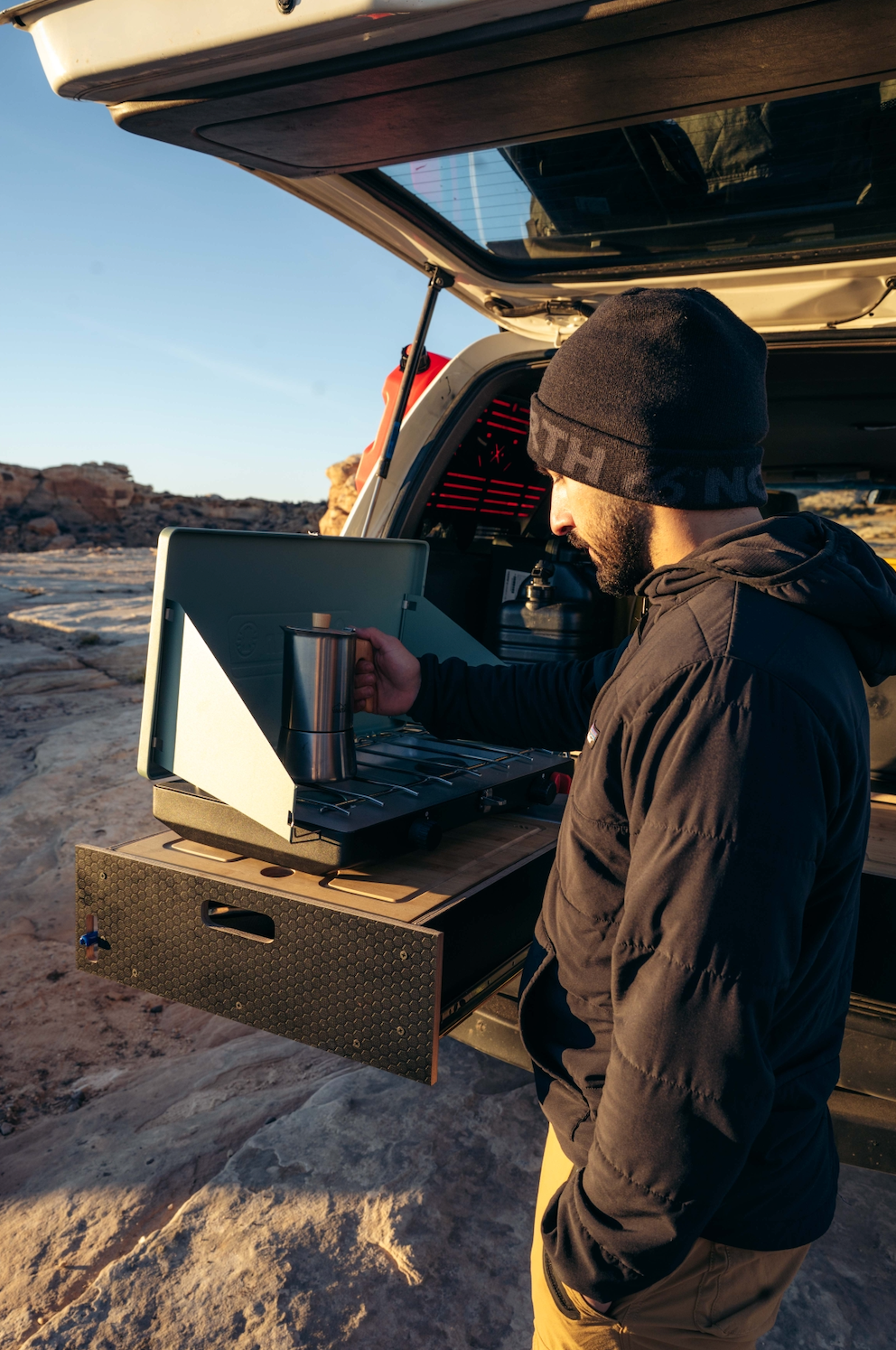 Man using camp stove on pull-out vehicle storage drawer outdoors