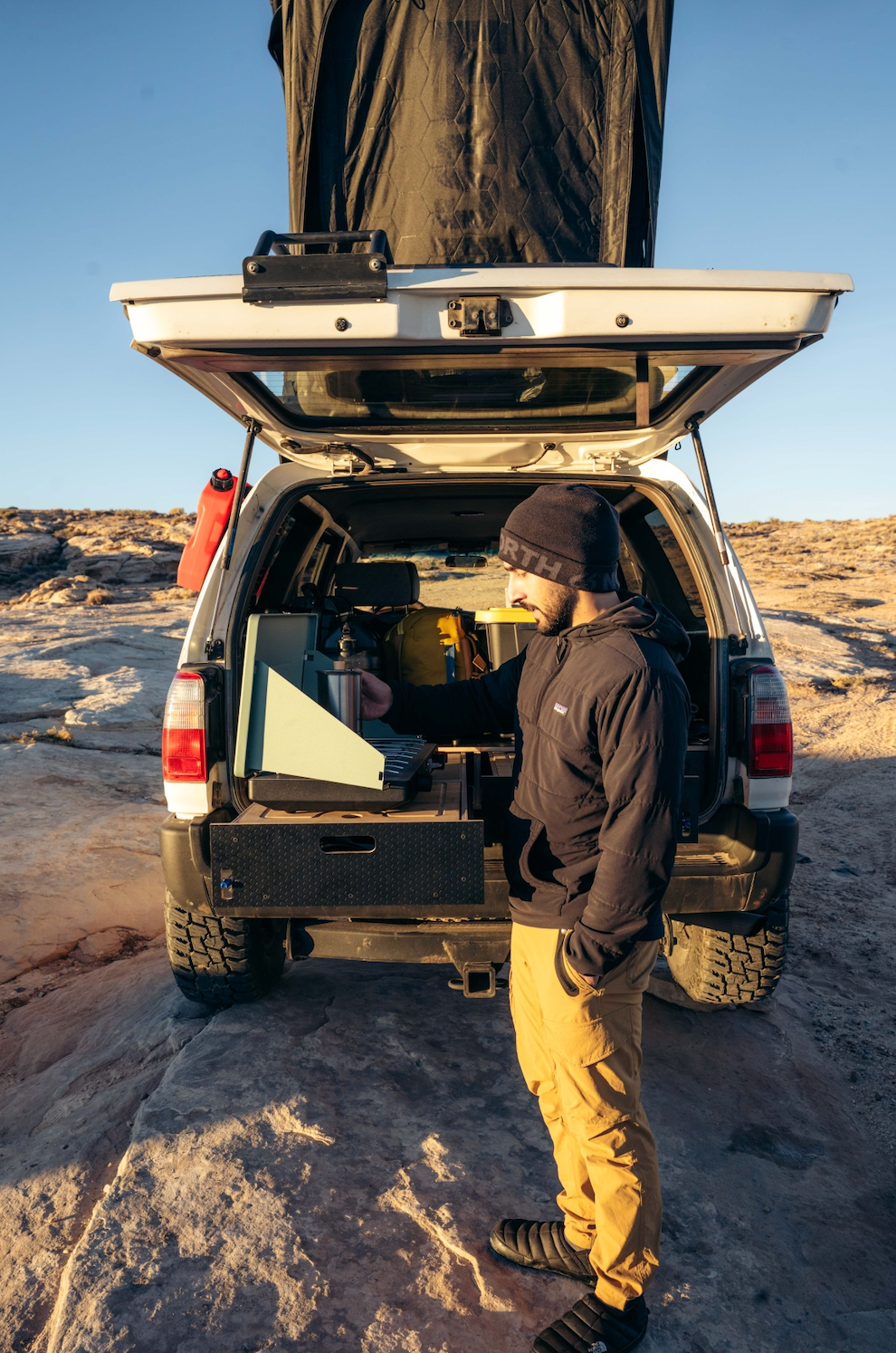 Man using a vehicle storage drawer system with camping gear in a desert landscape