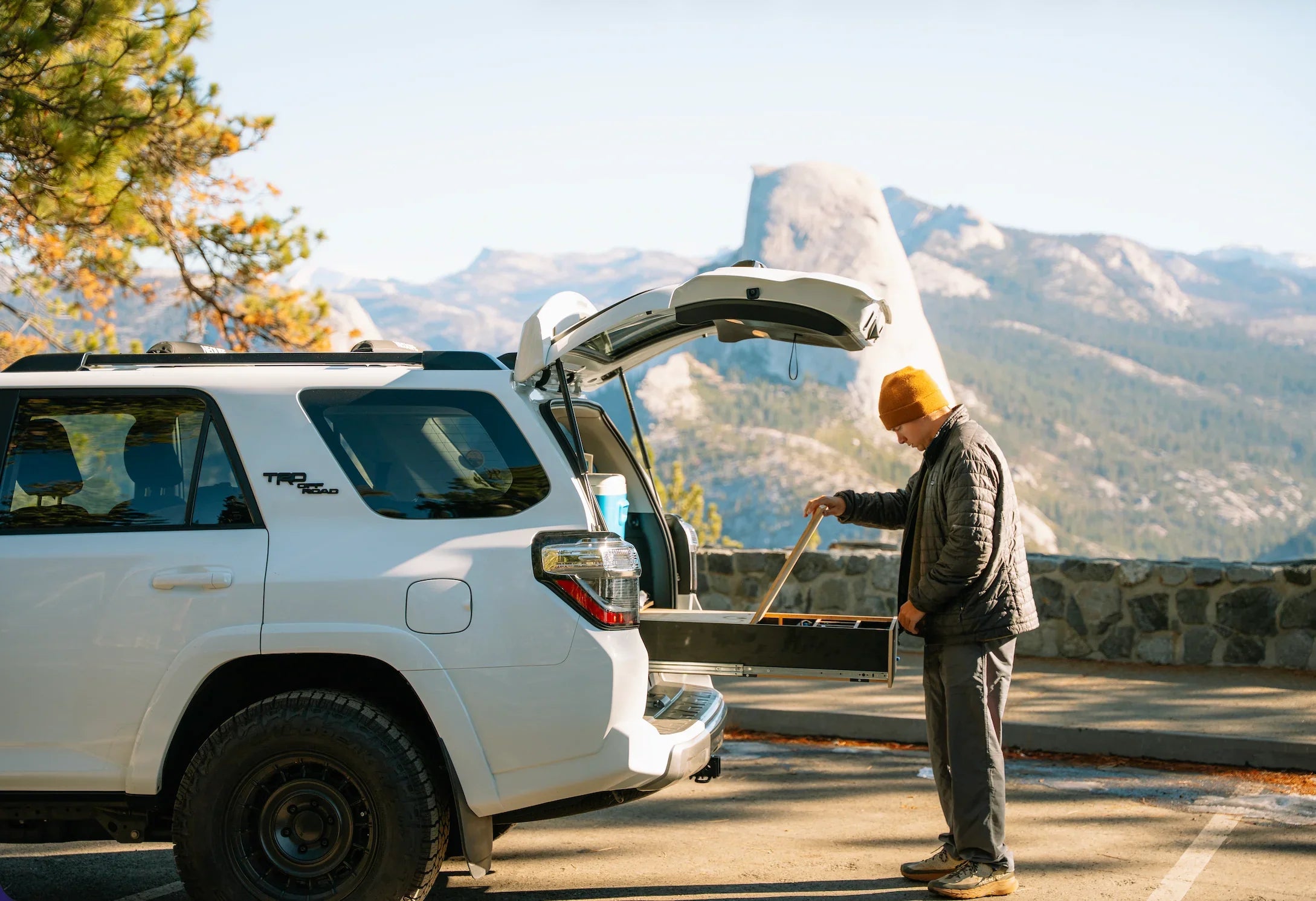 Man using vehicle storage drawer system outdoors with scenic mountain view