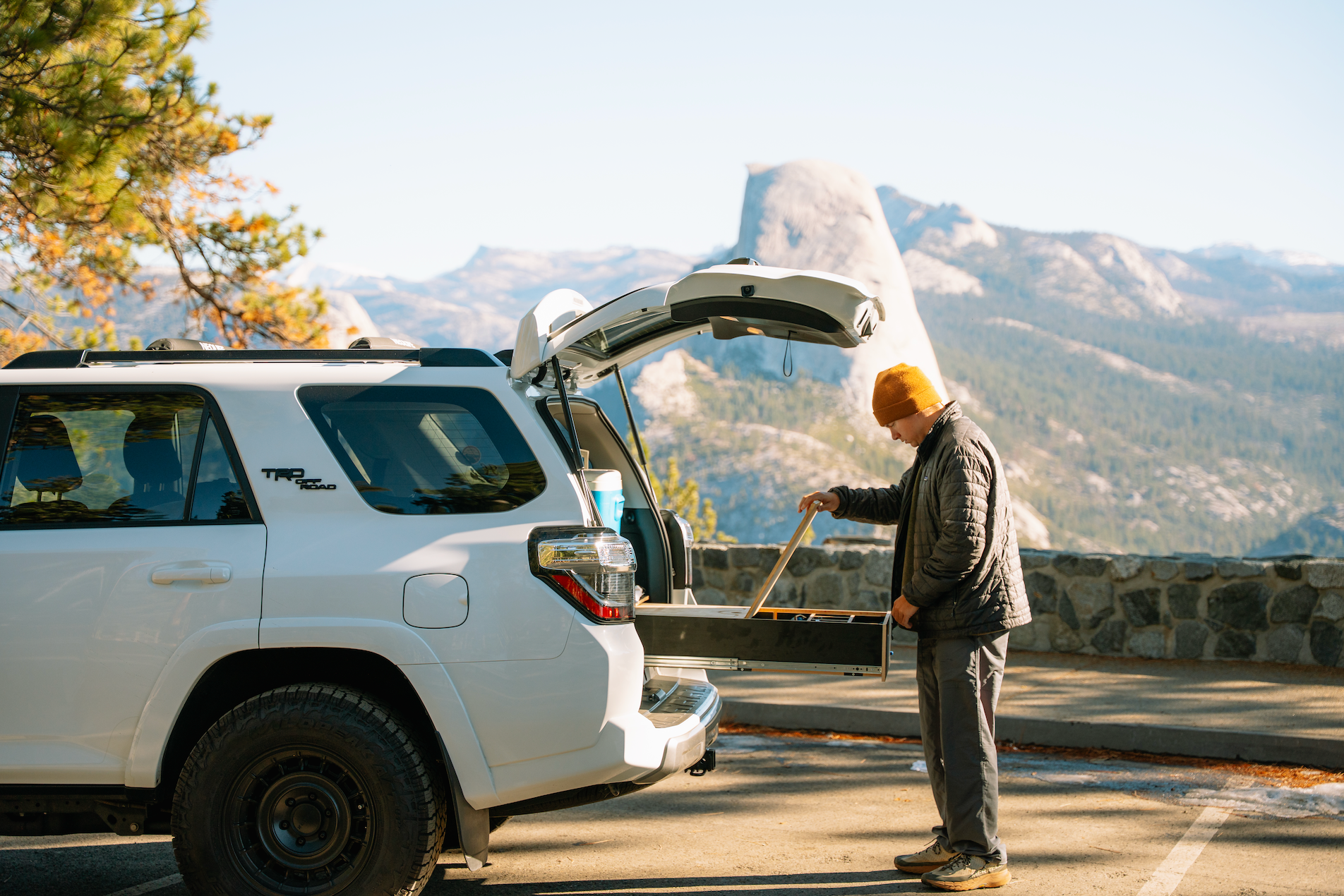 Man organizing SUV drawer storage system with mountain view in background