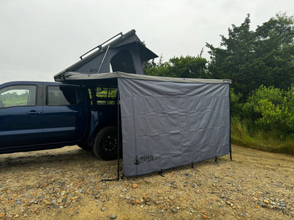 Pickup truck with rooftop tent and gray awning windbreaker set up outdoors