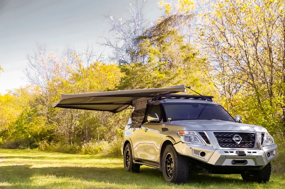 SUV with rooftop awning storage system parked outdoors in a wooded area