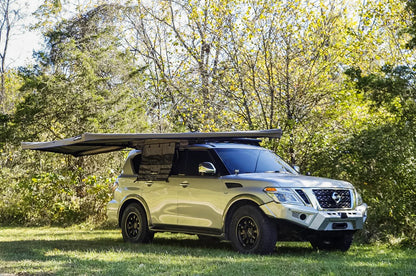 SUV equipped with a roof awning storage solution, parked outdoors in a wooded area.