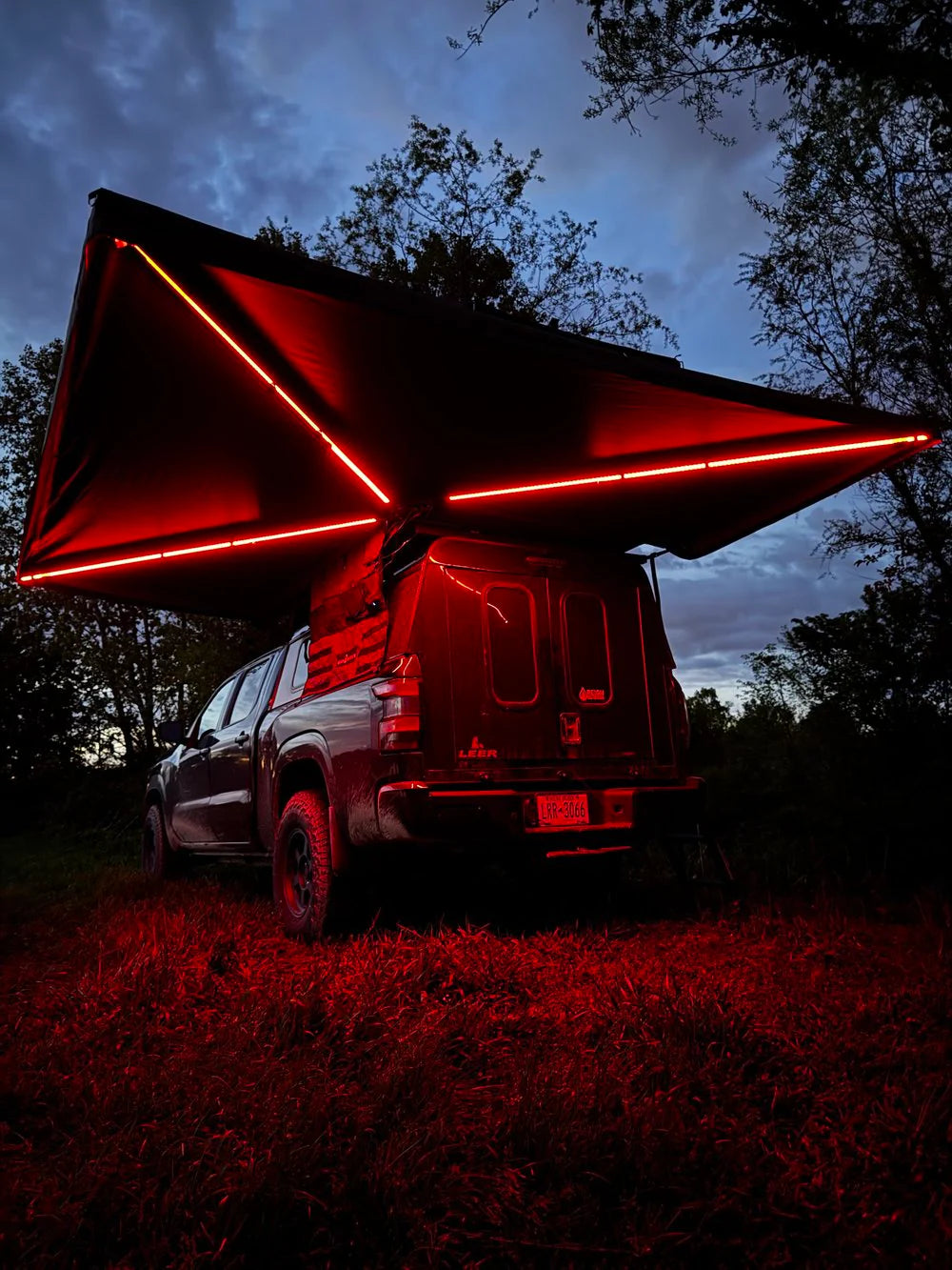Truck with red LED-lit awning parked outdoors at dusk, showcasing vehicle camping storage
