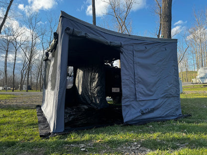 SUV with a gray outdoor awning tent setup for camping in a grassy park