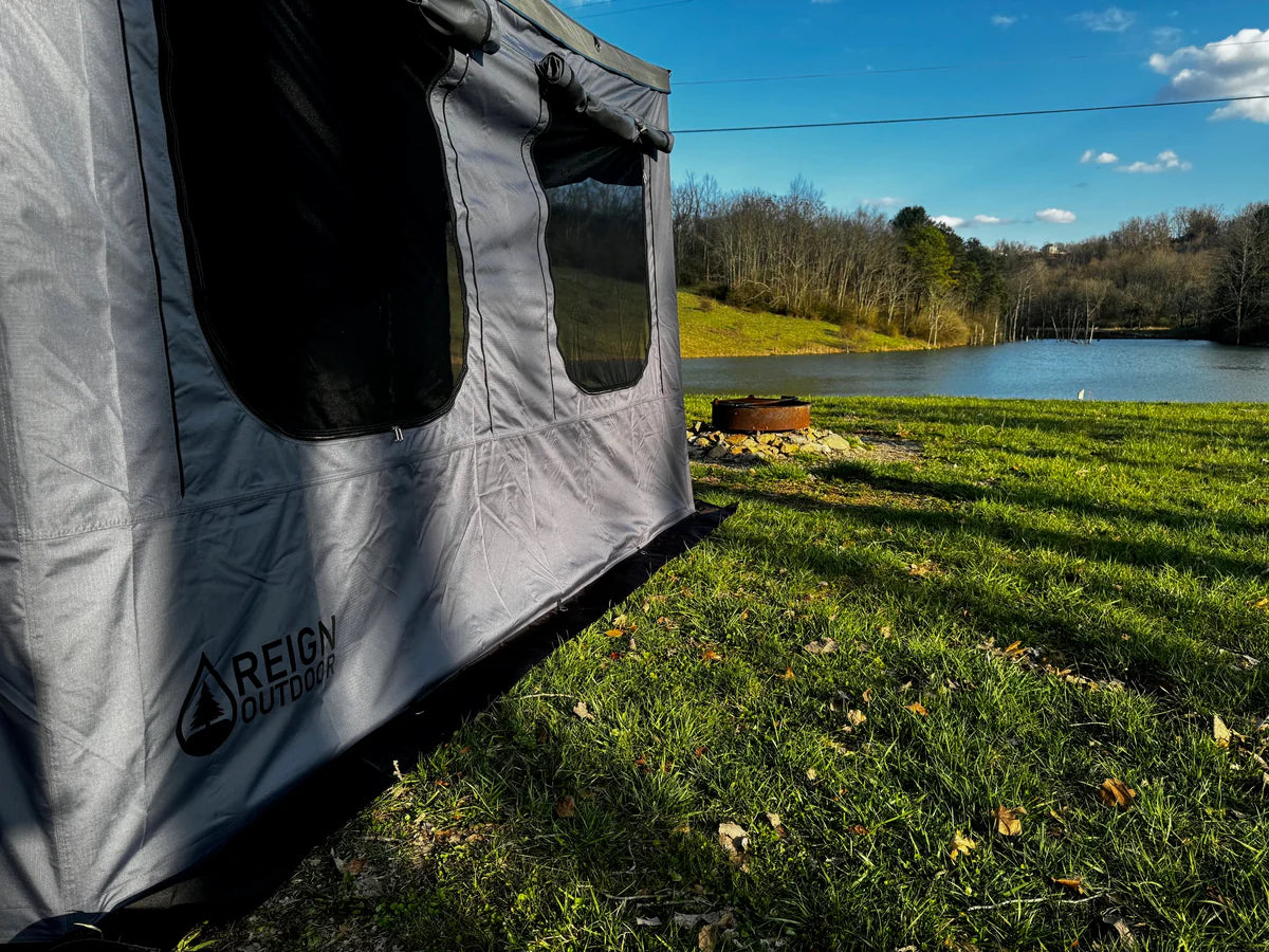 Outdoor camping tent with windows near a lake and fire pit on grassy area under blue sky